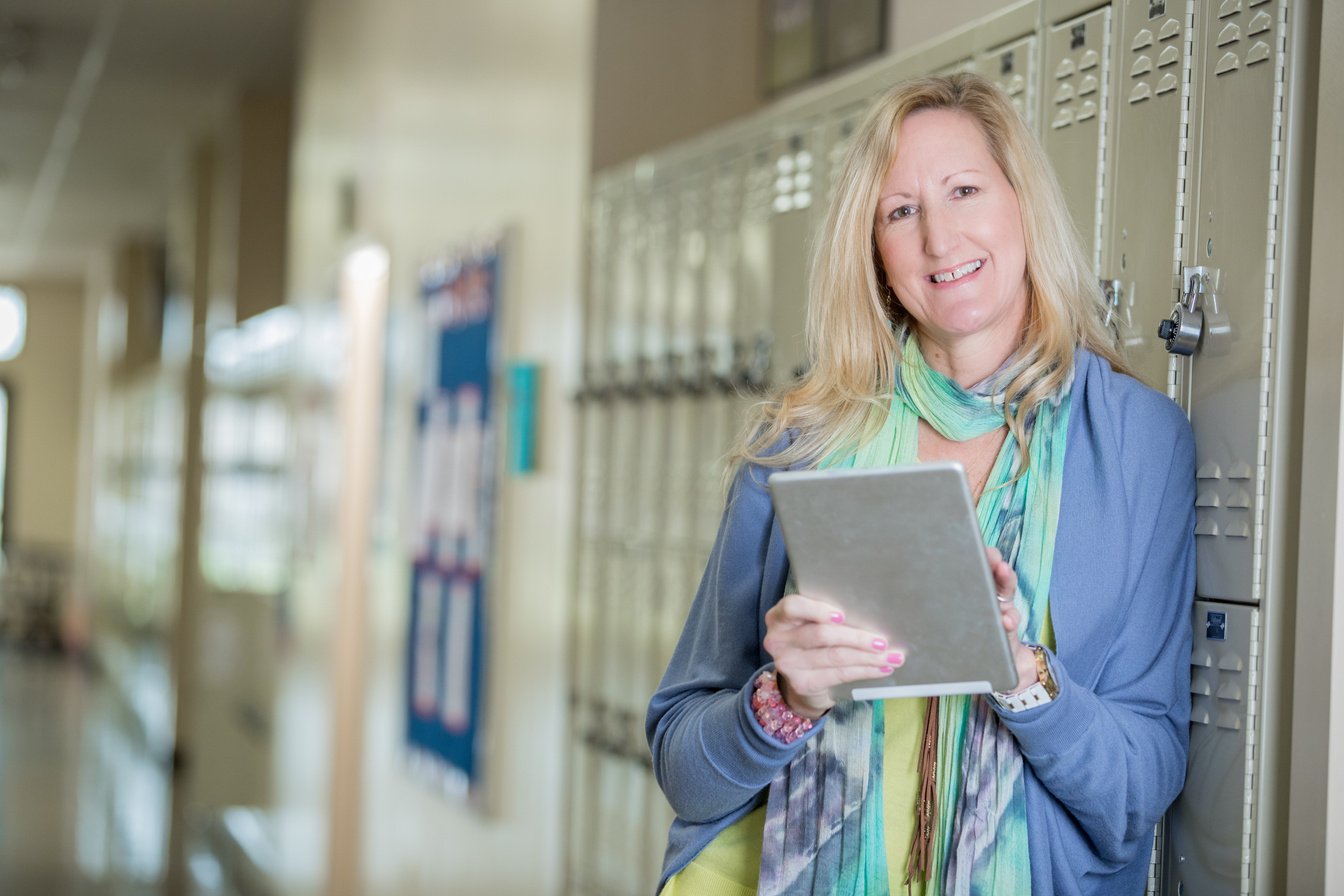 Principal of charter school standing by lockers and holding a digital tablet